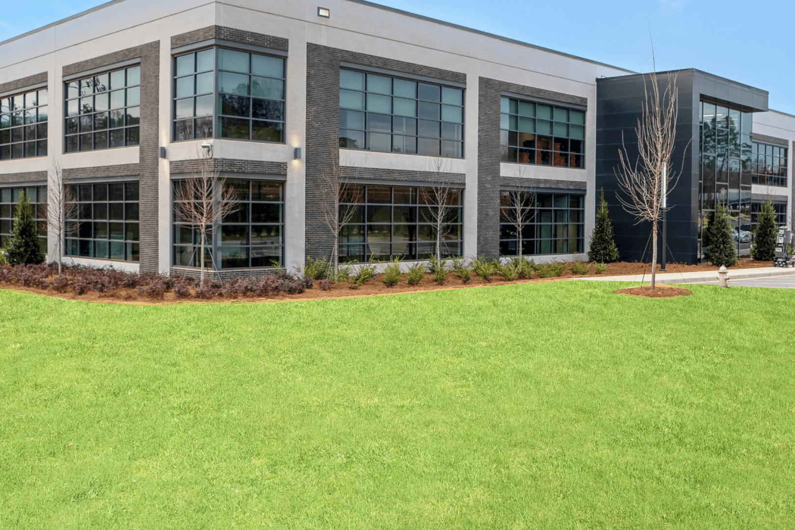 Modern Two-Story Commercial Building with Glass Windows Contemporary two-story commercial building exterior featuring large glass windows, dark brick accents, white stucco, and landscaped lawn with young trees.