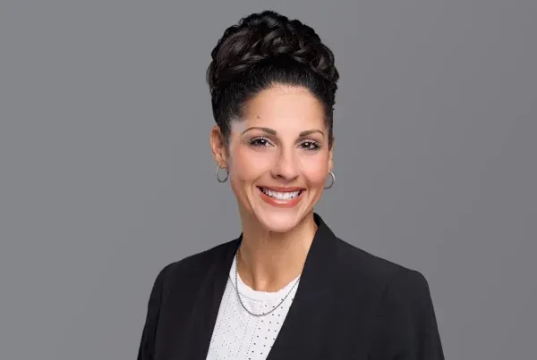 Professional headshot of Allison Floyd smiling, wearing a black blazer and white top against a gray background.