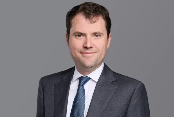 Professional headshot of Prince Matt wearing a dark suit and blue striped tie against a gray background