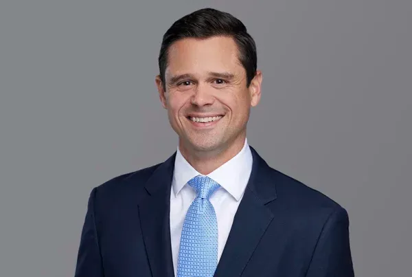 Professional headshot of Matt Probst smiling in a navy suit with light blue tie against gray background